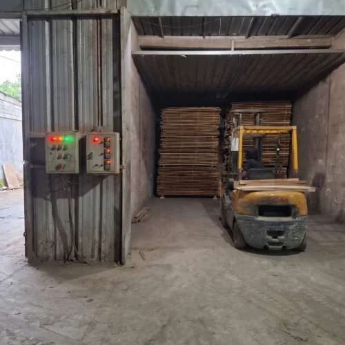 Forklift di depan oven kayu berisi tumpukan papan